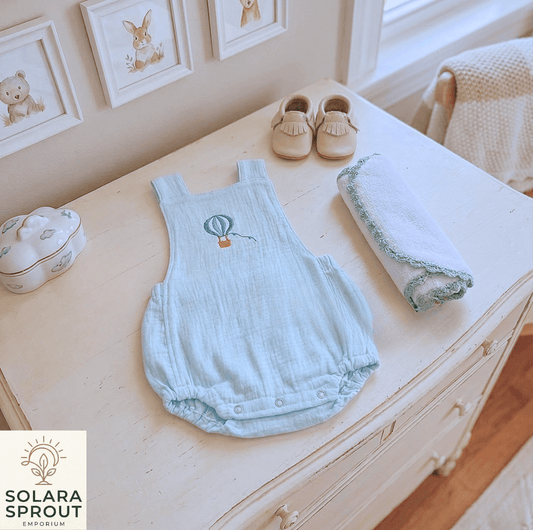 Hot Air Balloon Baby Muslin Romper displayed on a dresser with a towel and baby shoes.